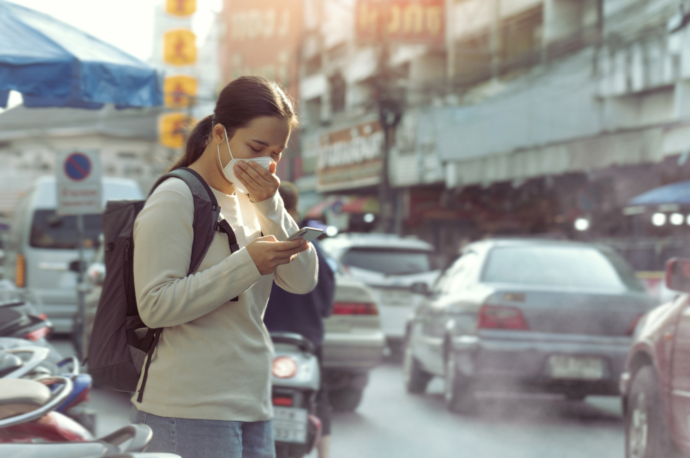 Zeigt eine Frau mit Mundschutz im dichten Stadtverkehr, die auf ihr Handy schaut